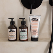 Abbildung der Bali Curls Deep Hydration Mask, des Moisturising Conditioners und dem Nourishing Shampoo auf der Ablage eines beigen Waschbeckens