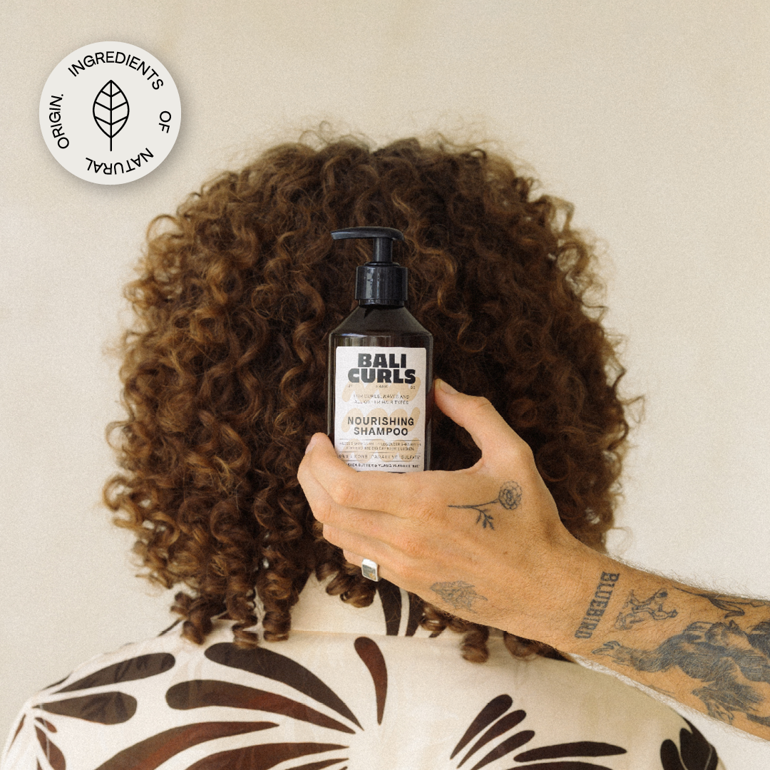 Abbildung der Bali Curls Nourishing Shampoos, in der Hand eines Tätowierten Mannes vor die Rückseite des Kopfes eines anderen Mannes mit schönem lockigen Haar und einem: "ingredients of Natural Origins" Sticker in der linken oberen Ecke