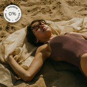 Abbildung einer Frau, die am Strand mit einem Seidentuch in der Sonne liegt und einem: "0% Parabene, Sulate und Silikone" Sticker in der linken oberen Ecke