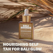 Bali Bronze Bronzing Drops Produktabbildung im Sand mit Palmenblatt im Hintergrund und dem Schriftzug: "Nourishing Self Tan for Bali Glow" darunter
